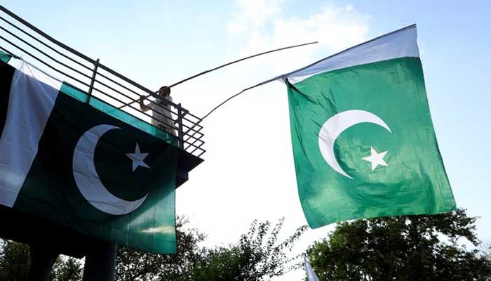 A boy uses a bamboo stick to adjust national flags at an overhead bridge ahead of Pakistans Independence Day, in Islamabad, August 10, 2018. — Reuters