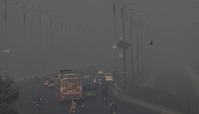 Commuters drive along a road amid dense smog in Lahore on December 11, 2025. — AFP