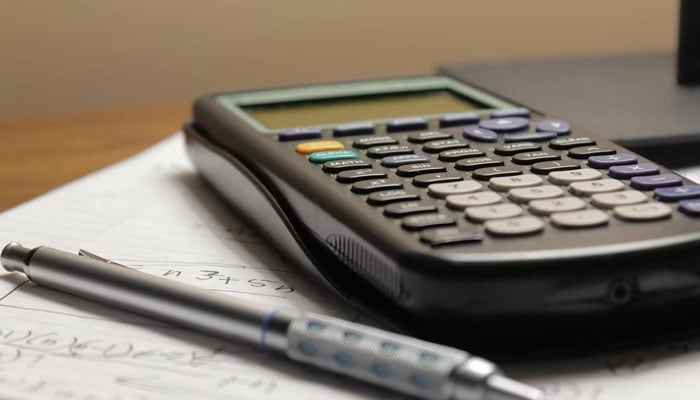 This representational image shows a calculator and a pen on a table. — Unsplash/File