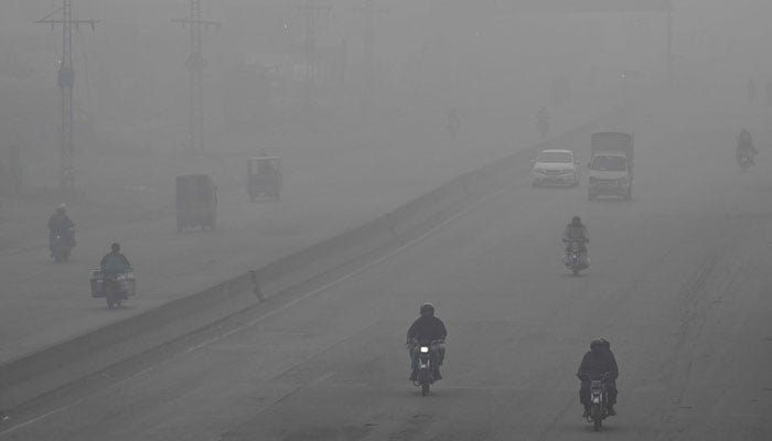 Commuters ride along a street amid dense smog in Lahore on December 14, 2025. — AFP