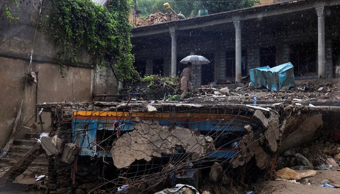 A resident walks with an umbrella to avoid rain at the damaged house, following a storm that caused heavy rains and flooding in Khyber Pakhtunkhwa on August 18, 2025. — Reuters