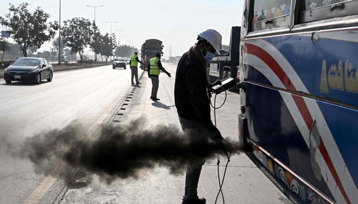This picture taken on December 10, 2025, shows technician Waleed Ahmed (R) examining a vehicle to test its emissions on the road, on the outskirts of Islamabad. — AFP