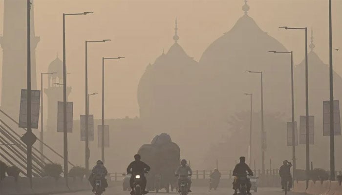 Commuters ride along a road amid smoggy conditions in Lahore on November 16, 2021. — AFP