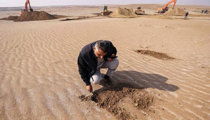 An Iraqi engineer examines the soil as excavators clear sand dunes and extract clay in the desert south of Samawah on December 21, 2025. —AFP