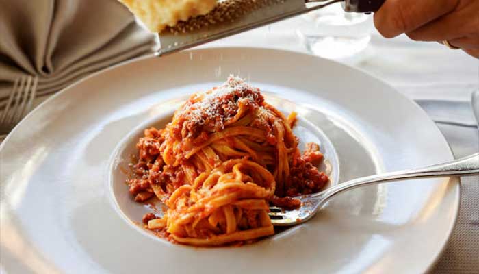 A person grates parmesan cheese over a plate of fettuccine with ragu at a restaurant in Rome, Italy, March 25, 2024. — Reuters