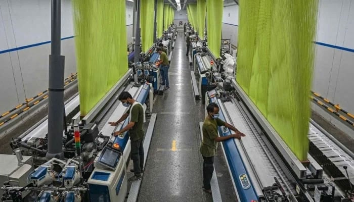 This representational image shows workers operating a machine preparing fabric at a textile mill. — AFP/File