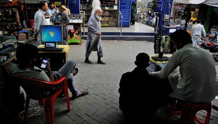 Men sit at their computers waiting to load media files into mobile phones for customers in the Abpara market in Islamabad, Pakistan, on October 20, 2017. — Reuters