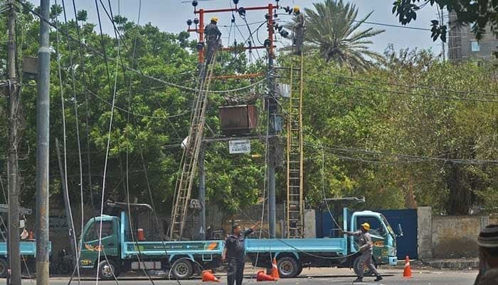 Men work on electric pylons along the roadside in Karachi on May 30, 2021. — AFP