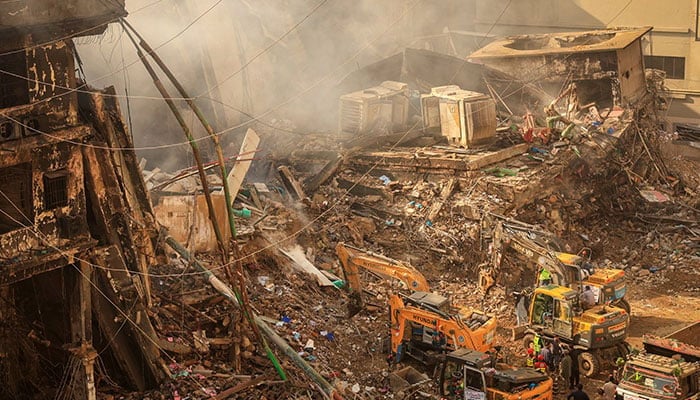 Emergency personnel stand as heavy machinery clears the site following a massive fire that broke out in the Gul Plaza Shopping Mall in Karachi on January 20, 2026. — Reuters