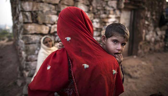 A woman, whose family moved to Islamabad from Khyber-Pakhtunkhwa province to look for work, holds her son while talking to her neighbour outside her house on the outskirts of Islamabad. — Reuters/File