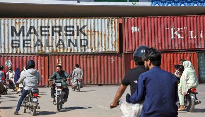 Commuters look at containers placed to block a road. — Online/File