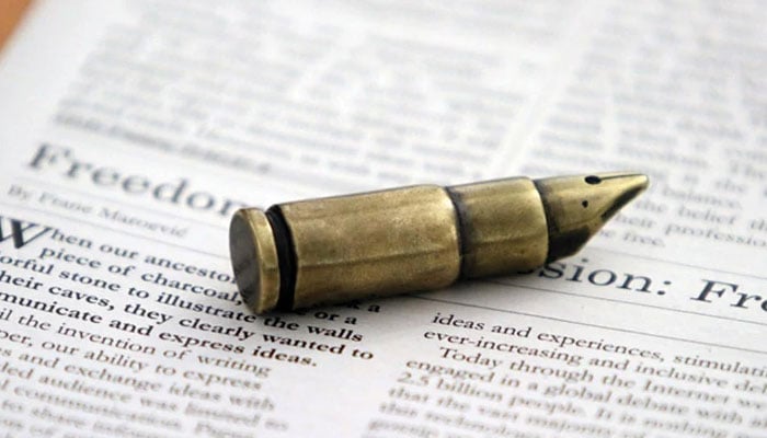 The representational image displays a small, metallic object resembling a pen nib shaped like a bullet, resting on a newspaper page that shows Freedom of Expression written on it. — The News/File