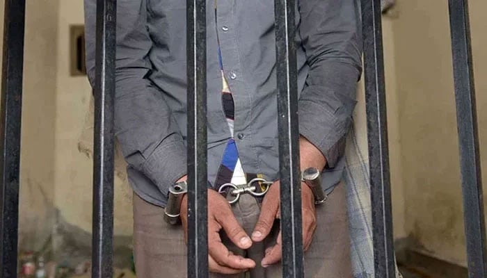 A representational image of a person handcuffed behind bars. — AFP/File