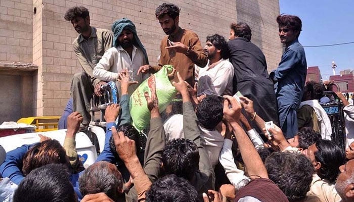 People attempt to get of hold of ration bags during distribution of Ramazan package. — APP/File