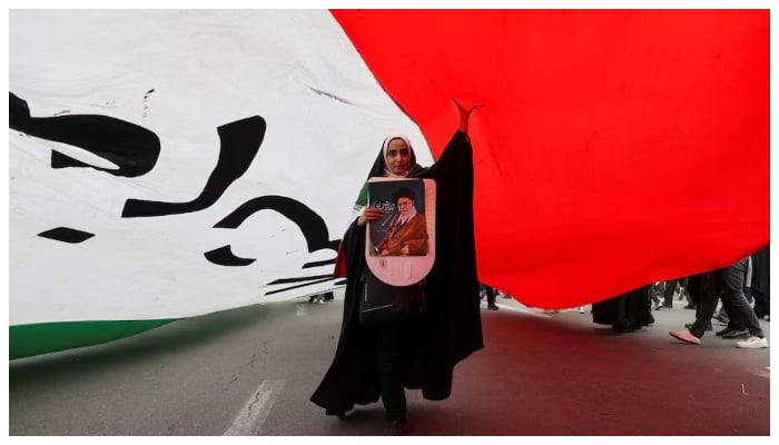 An Iranian woman holding a poster depicting Irans Supreme Leader Ayatollah Ali Khamenei walks under a large flag during the 47th anniversary of the Islamic Revolution in Tehran, Iran February 11, 2026.—Reuters