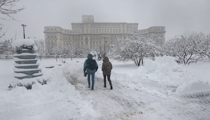 People walk through a snow‑covered park with the Palace of the Parliament in the background after a snowstorm in Bucharest, Romania, February 18, 2026.     — Reuters