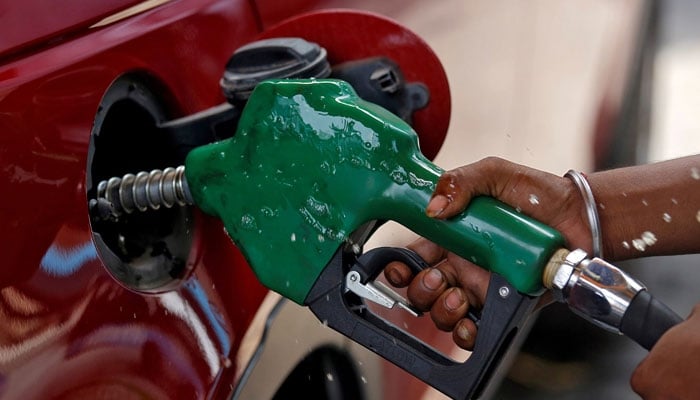 A worker holds a nozzle to pump petrol into a vehicle at a fuel station. — Reuters/File