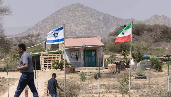 People walk by the flags of Israel and Somaliland flying alongside each other at the entrance to a fruit farm between the capital city of Hargeisa and Port city of Berbera. —AFP/File