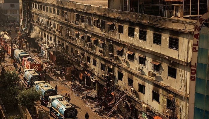 Fire department workers walk past the site, following a massive fire that broke out in the Gul Plaza shopping centre in Karachi on January 20, 2026. — Reuters