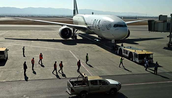 Ground staff stand next to the Pakistan International Airlines (PIA) aircraft ahead of its takeoff for Paris at the Islamabad International Airport on January 10, 2025. — INP