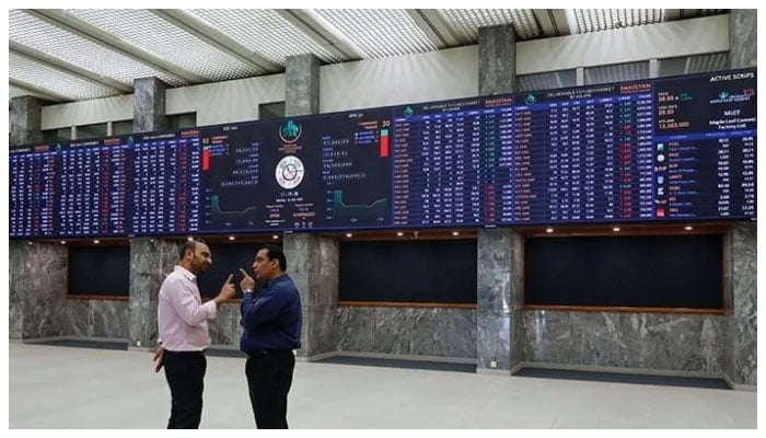 Two investors can be seen discussing in front of the digital stock board at the Pakistan Stock Exchange. — AFP/File