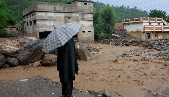 A resident stands with an umbrella as rainwater flowing from mountains crosses a damaged area, following a storm that caused heavy rains and flooding in Khyber Pakhtunkhwa on August 18, 2025. — Reuters