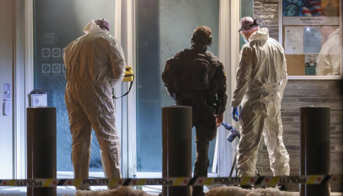 Forensic experts and a police officer stand in front the entrance of the US embassy after a loud bang was reported during the night with no injuries reported in Oslo on March 8, 2026. —AFP