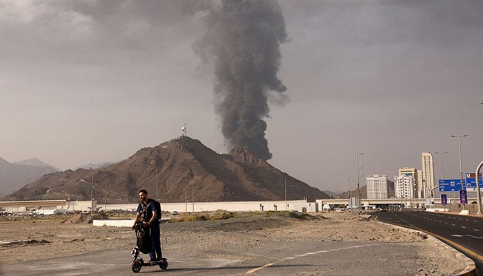 A person rides on a scooter as smoke rises in the Fujairah oil industry zone following a fire caused by debris after interception of a drone by air defenses, in Fujairah, United Arab Emirates, March 3, 2026. — Reuters
