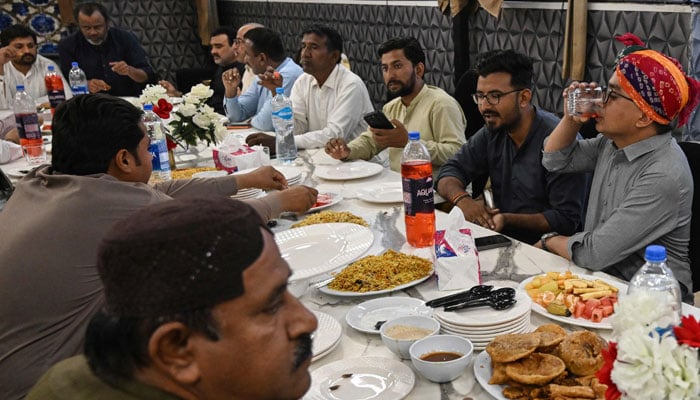 This photograph, taken on February 27, 2026, shows Hindu and Muslim men enjoying a meal as they break their fast during the Islamic holy fasting month of Ramadan, at Mithi in the Tharparkar district of Sindh province. — AFP