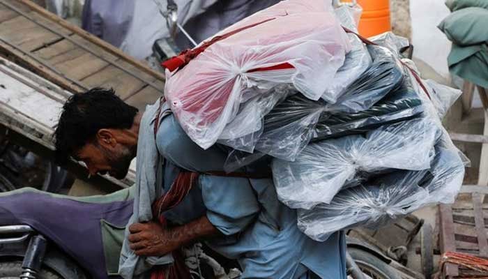 A labourer bends over as he carries packs of textile fabric on his back to deliver to a nearby shop in a market in Karachi. — Reuters/File