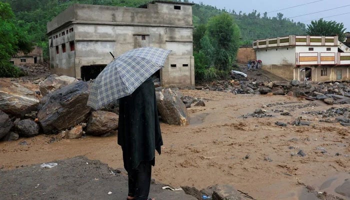 This representational image shows a resident standing with an umbrella as rainwater flowing from mountains crosses a damaged area, following a storm that caused heavy rains and flooding in Khyber Pakhtunkhwa on August 18, 2025. — Reuters