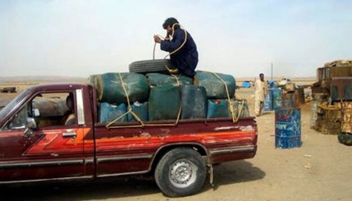 A man sits on top of plastic canisters of petrol that he says was brought from Iran, as he prepares to unload them from a van at a roadside shop near a Pakistan and Iran border, February 20, 2013. — Reuters