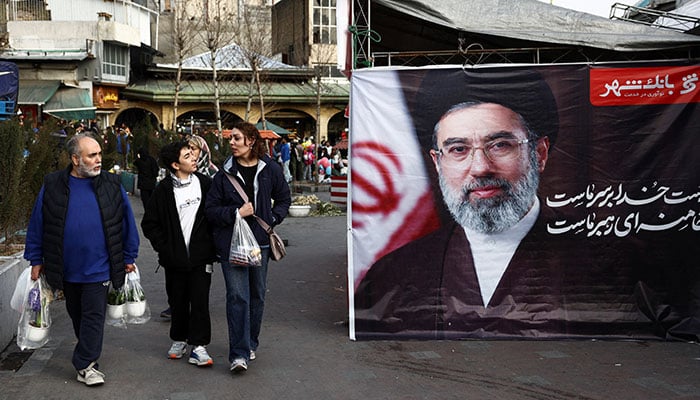 People walk next to a banner with a picture of Irans new Supreme Leader, Mojtaba Khamenei, at Tajrish Bazaar, ahead of Nowruz, the Iranian New Year, amid the U.S.-Israeli conflict with Iran, in Tehran, Iran, March 19, 2026. — Reuters