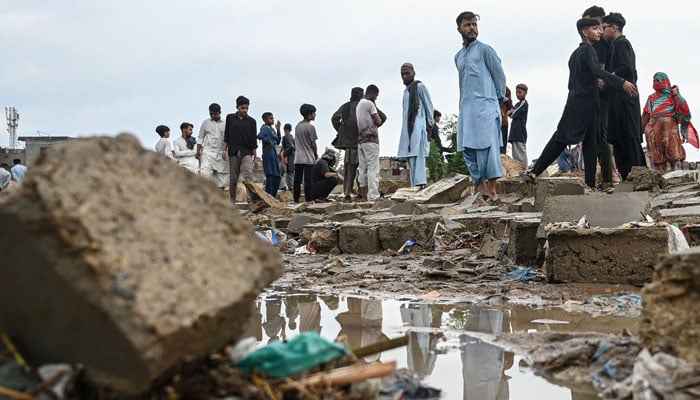 Residents stand near the debris of a collapsed wall following heavy rain and strong winds in Karachi on March 19, 2026. — AFP
