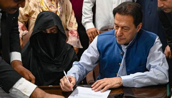 Pakistan Tehreek-e-Insaf (PTI) founder Imran Khan (right), along with his wife Bushra Bibi, signs surety bonds for bail in various cases at a registrars office in the Lahore High Court, July 17, 2023. — AFP