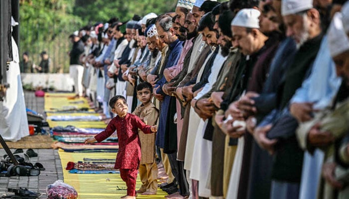Children look at Muslim devotees offering Eid al-Fitr prayers in Rawalpindi on March 21, 2026. — AFP