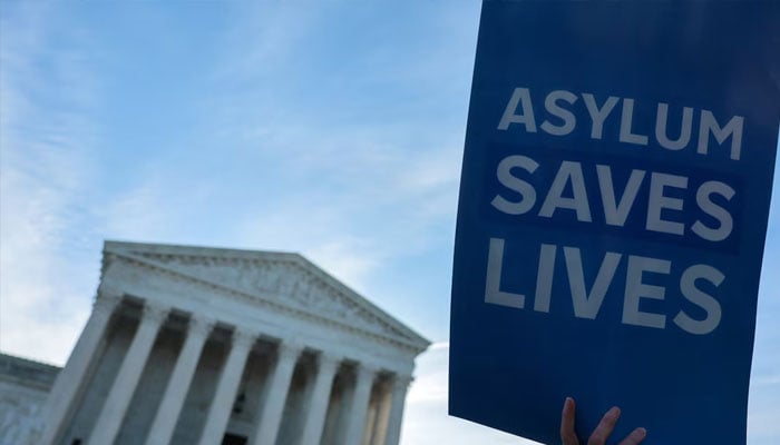 A demonstrator holds a sign as a small group of clergy gather for a vigil prior to arguments in Noem v. Al Otro Lado, a case to determine if noncitizens blocked on the Mexican side of the border by U.S. officials can apply for asylum, at the US Supreme Court building in Washington, DC, US, March 24, 2026.—Reuters