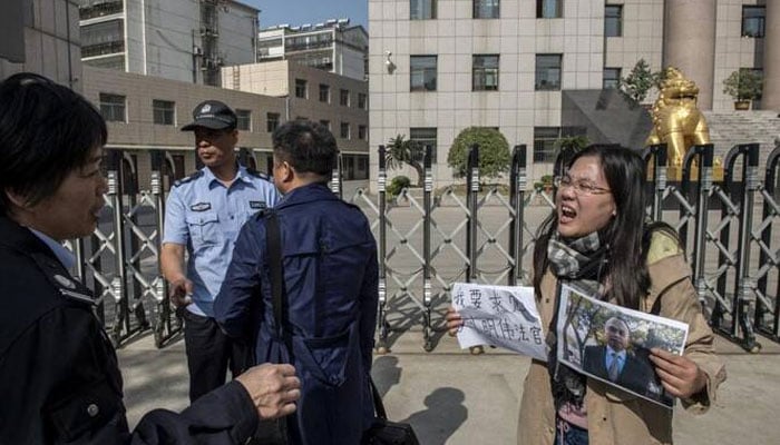 This photo taken on October 31, 2019 shows Xu Yan (R), wife of human rights lawyer Yu Wensheng, holding a piece of paper the reads I want to request a meeting with Judge Liu Mingwei and a picture of her husband as she stands next to one of her lawyers Xie Yang (C-in dark blue) as security personnel (L) ask them to move away outside the Xuzhou Intermediate People’s Court in Xuzhou. —AFP