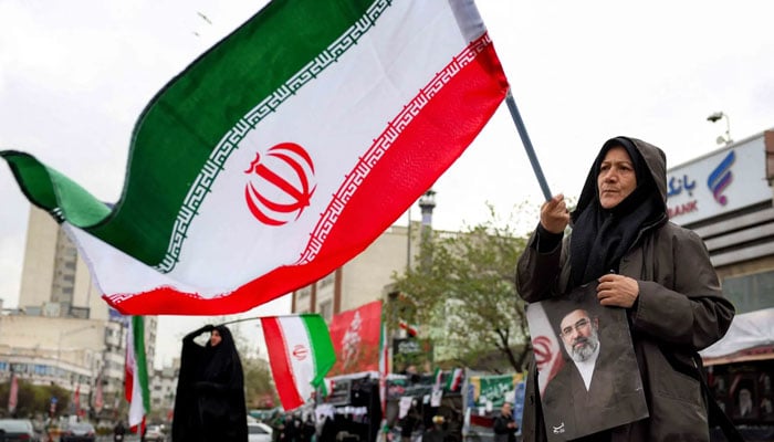 A woman holds a picture of Iran’s new Supreme Leader Mojtaba Khamenei while waving a national flag in central Tehran on March 25, 2026. — AFP