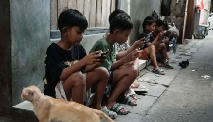 Children play online games against each other on smartphones and tablets along an alley in Jakarta on March 26, 2026. — AFP