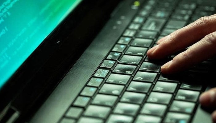 A person types on a laptop keyboard, with code visible on the screen. — AFP