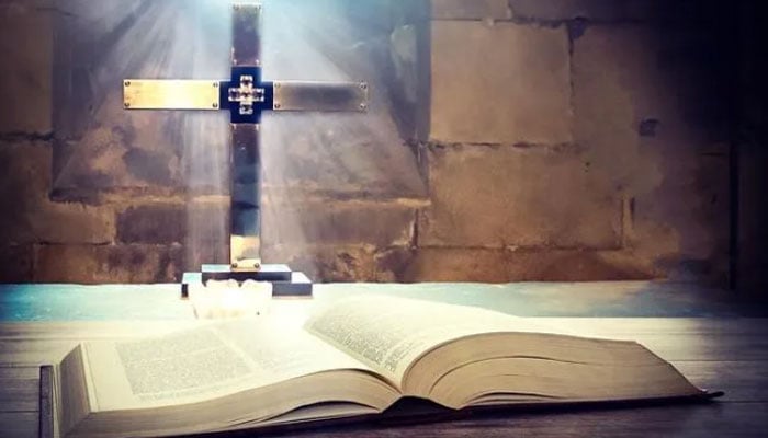 This representational image shows a large, open book, specifically a Holy Bible, resting on a wooden surface in front of a shining cross. — AFP/File