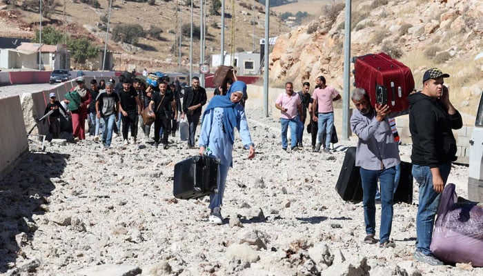 People carry their belongings while walking on the rubble, after an Israeli strike, as they flee Lebanon due to ongoing hostilities between Hezbollah and Israeli forces, at Masnaa border crossing with Syria, in Lebanon, October 4, 2024. — Reuters