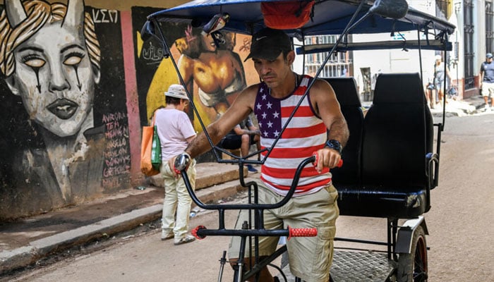 A man wearing a US-flag designed T-shirt rides his tricycle along a street in Havana. —AFP/File