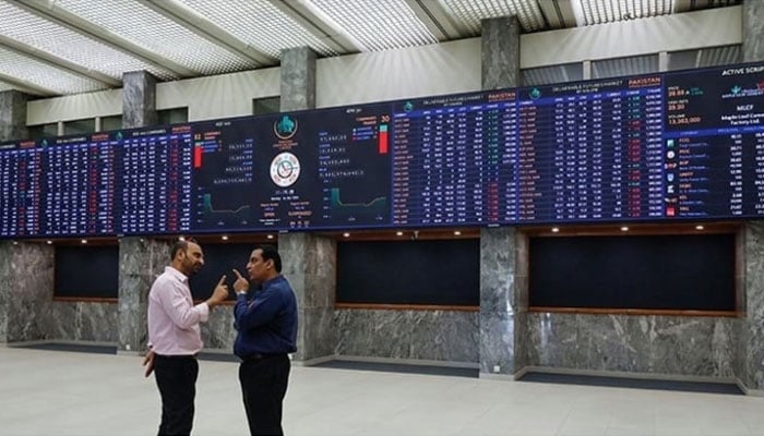 Two investors can be seen discussing in front of the digital stock board at the Pakistan Stock Exchange. — AFP/File
