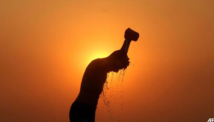 A labourer is silhouetted against the setting sun as he bathes on a hot summer day on Jun 1, 2024. — AFP