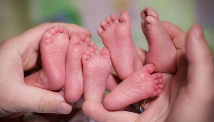A representational image showing a person holding up the feet of three babies. — Pexels/File