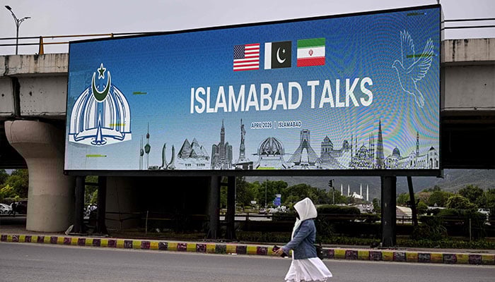 A woman walks past a digital screen displaying news of US-Iran peace talks along a road in Islamabad on April 10, 2026. — AFP