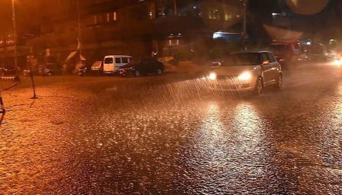 The image shows vehicles passing through accumulated rain water during rain in Karachi. — INP/File