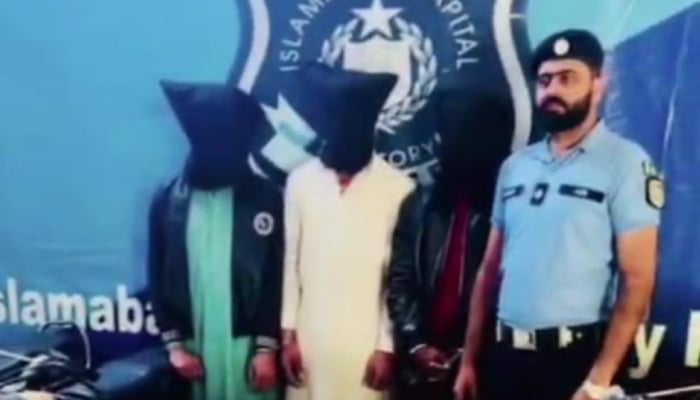 An Islamabad police officer posing for photo beside arrested culprits. —APP/File